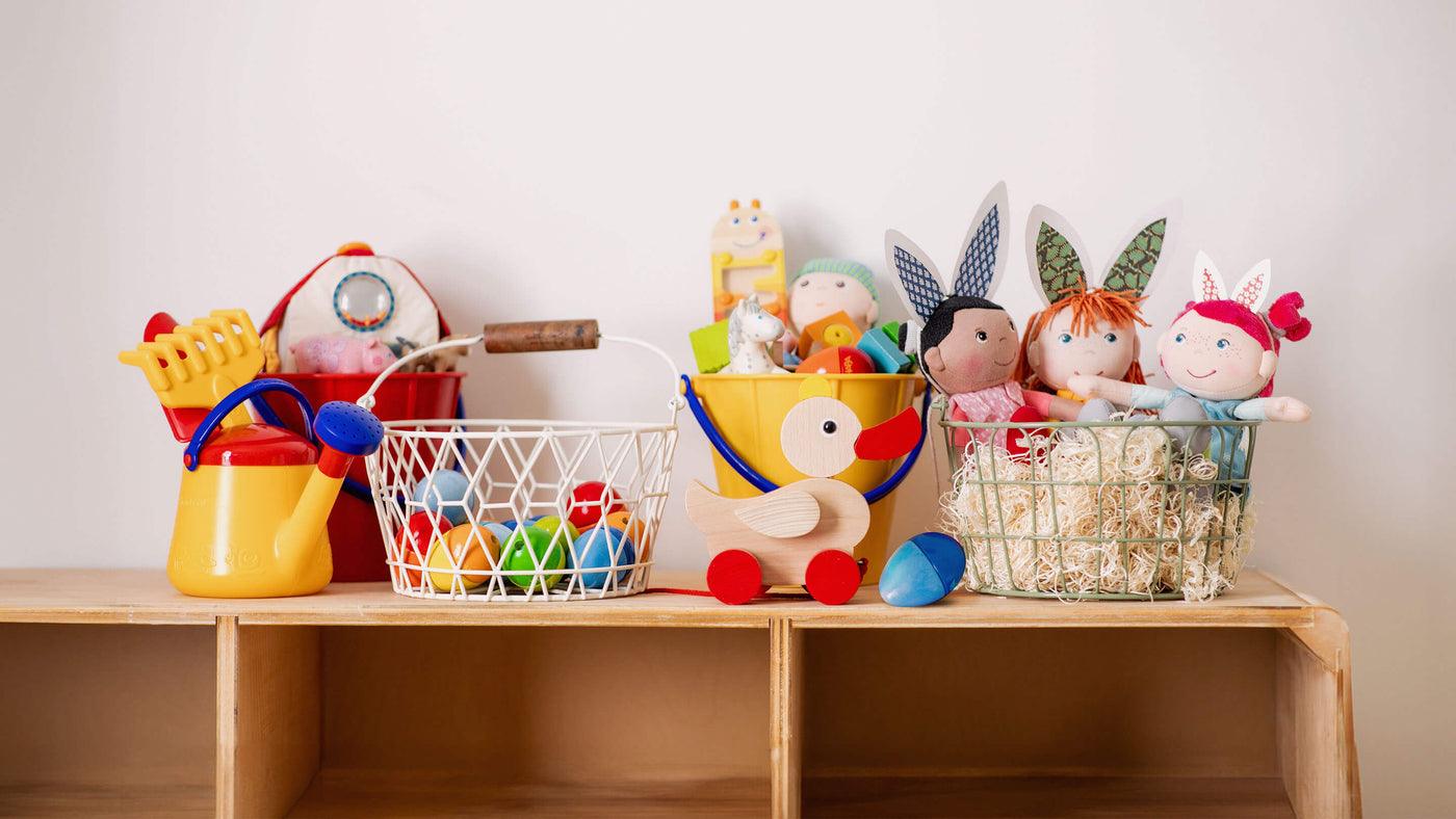 HABA watering can, basket with wooden eggs, wooden duck, musical instruments, and dolls on top of a playshelf
